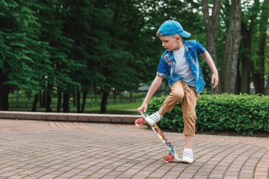 Bir küçük şehir çocuğu ve bir kaykay. Genç bir adam bir parkta bir kaykay üzerinde biniyor. City Style. Şehir çocukları. Bir çocuk bir kaykay binmek öğrenir