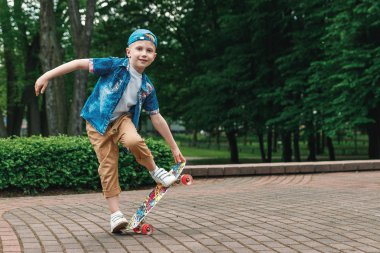 Bir küçük şehir çocuğu ve bir kaykay. Genç bir adam bir parkta bir kaykay üzerinde biniyor. City Style. Şehir çocukları. Bir çocuk bir kaykay binmek öğrenir