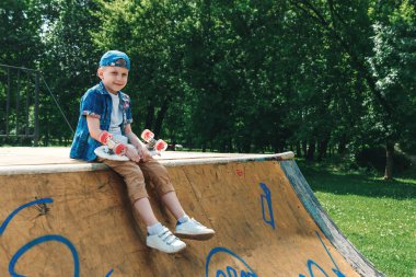 Bir küçük şehir çocuğu ve bir kaykay. Genç bir adam parkta duran ve bir kaykay tutarak. City Style. Şehir çocukları. Bir çocuk bir kaykay binmek öğrenir