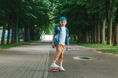 Bir küçük şehir çocuğu ve bir kaykay. Genç bir adam bir parkta bir kaykay üzerinde biniyor. City Style. Şehir çocukları. Bir çocuk bir kaykay binmek öğrenir