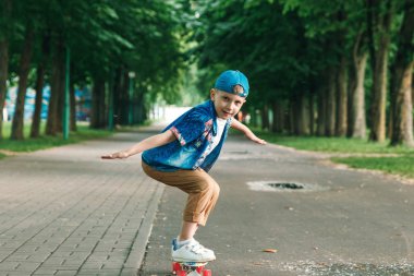 Bir küçük şehir çocuğu ve bir kaykay. Genç bir adam bir parkta bir kaykay üzerinde biniyor. City Style. Şehir çocukları. Bir çocuk bir kaykay binmek öğrenir