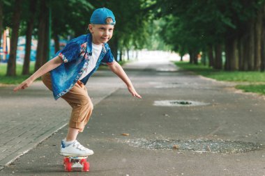 Bir küçük şehir çocuğu ve bir kaykay. Genç bir adam bir parkta bir kaykay üzerinde biniyor. City Style. Şehir çocukları. Bir çocuk bir kaykay binmek öğrenir