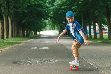 Bir küçük şehir çocuğu ve bir kaykay. Genç bir adam bir parkta bir kaykay üzerinde biniyor. City Style. Şehir çocukları. Bir çocuk bir kaykay binmek öğrenir