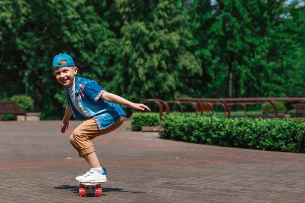 A small city boy and a skateboard. A young guy is riding in a park on a skateboard. City Style. City children. A child learns to ride a skateboard