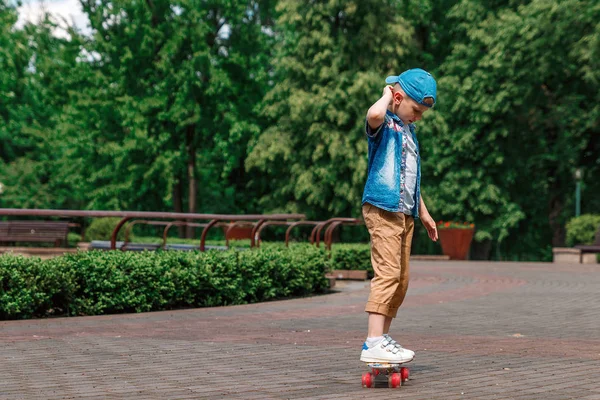 A small city boy and a skateboard. A young guy is riding in a park on a skateboard. City Style. City children. A child learns to ride a skateboard