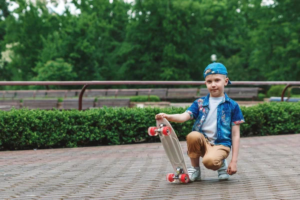 A small city boy and a skateboard. A young guy is riding in a park on a skateboard. City Style. City children. A child learns to ride a skateboard