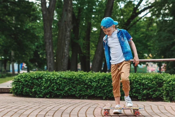 Bir küçük şehir çocuğu ve bir kaykay. Genç bir adam bir parkta bir kaykay üzerinde biniyor. City Style. Şehir çocukları. Bir çocuk bir kaykay binmek öğrenir