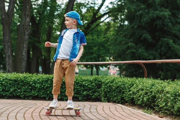 A small city boy and a skateboard. A young guy is riding in a park on a skateboard. City Style. City children. A child learns to ride a skateboard