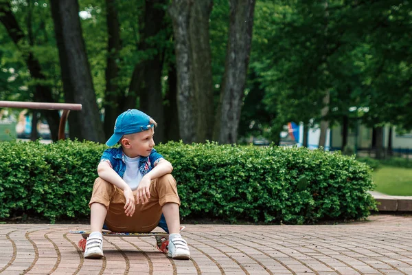 A small city boy and a skateboard. A young guy is riding in a park on a skateboard. City Style. City children. A child learns to ride a skateboard