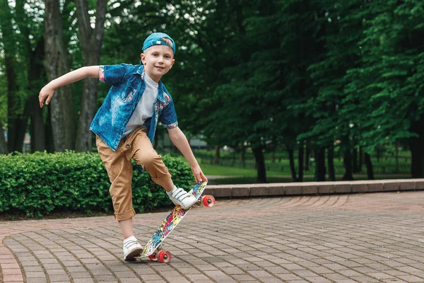 Bir küçük şehir çocuğu ve bir kaykay. Genç bir adam bir parkta bir kaykay üzerinde biniyor. City Style. Şehir çocukları. Bir çocuk bir kaykay binmek öğrenir