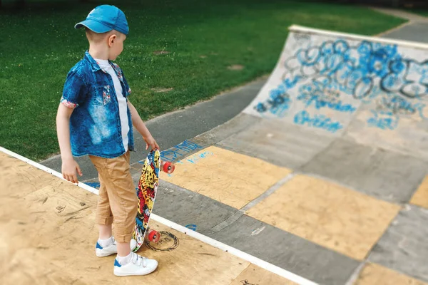 A small city boy and a skateboard. A young guy is riding in a park on a skateboard. City Style. City children. A child learns to ride a skateboard