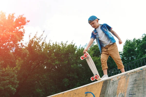 A small city boy and a skateboard. A young guy is riding in a park on a skateboard. City Style. City children. A child learns to ride a skateboard