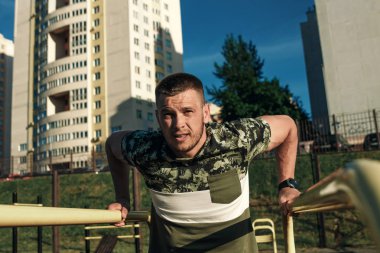 Stadyumdaki düzensiz barlarda egzersiz yapan genç adam, sporcu, şehirdeki açık hava eğitimi.