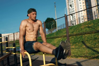 Genç bir adam bir spor zemin, bir atlet, şehirde bir basın egzersiz eğitim açık bacaklarına yükseltir