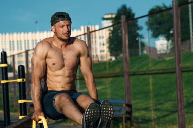 Genç bir adam bir spor zemin, bir atlet, şehirde bir basın egzersiz eğitim açık bacaklarına yükseltir