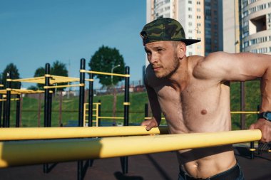 Stadyumdaki düzensiz barlarda egzersiz yapan genç adam, sporcu, şehirdeki açık hava eğitimi.