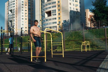 Stadyumdaki düzensiz barlarda egzersiz yapan genç adam, sporcu, şehirdeki açık hava eğitimi.