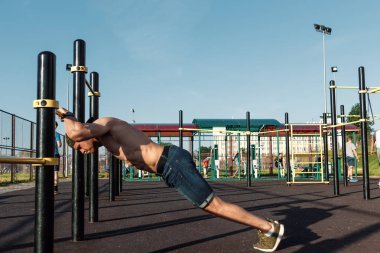 Stadyumdaki düzensiz barlarda egzersiz yapan genç adam, sporcu, şehirdeki açık hava eğitimi.