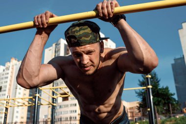 Stadyumdaki düzensiz barlarda egzersiz yapan genç adam, sporcu, şehirdeki açık hava eğitimi.