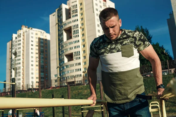 Stadyumdaki düzensiz barlarda egzersiz yapan genç adam, sporcu, şehirdeki açık hava eğitimi.