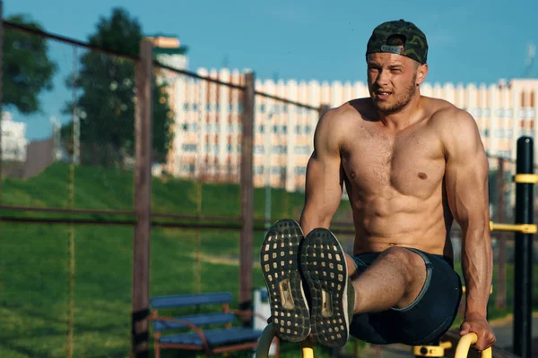 Genç bir adam bir spor zemin, bir atlet, şehirde bir basın egzersiz eğitim açık bacaklarına yükseltir