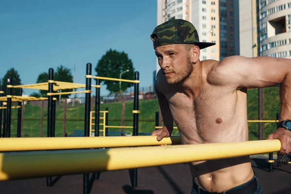 Stadyumdaki düzensiz barlarda egzersiz yapan genç adam, sporcu, şehirdeki açık hava eğitimi.