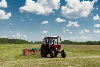 Tarım makineleri, mavi gökyüzü karşı bir alanda ot toplama bir traktör. Hasat saman, hasat çimen. Sezon hasat, çim, tarım arazisi.