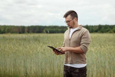 Bir çiftçi alanında ayakta ve tablet kullanma dostum. Modern tarım teknolojileri uygulama. Tarım arazisi, yeni teknolojiler, hasat, gübreleme, Ürün İnceleme.