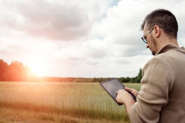 Bir çiftçi alanında ayakta ve tablet kullanma dostum. Modern tarım teknolojileri uygulama. Tarım arazisi, yeni teknolojiler, hasat, gübreleme, Ürün İnceleme.