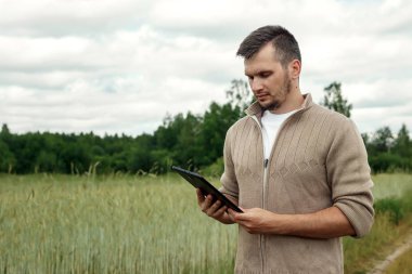 Bir çiftçi alanında ayakta ve tablet kullanma dostum. Modern tarım teknolojileri uygulama. Tarım arazisi, yeni teknolojiler, hasat, gübreleme, Ürün İnceleme.