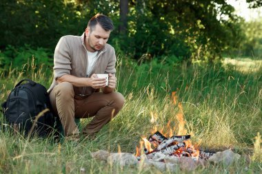 Açık havada şömine başında bir adam oturuyor. Yaz tatil kavramı. Adam uzun yürüyüşe çıkan kimse yapmak orman yangında. Ekoloji, çevre, doğa. Kamp, hiking, yaşam biçimi.