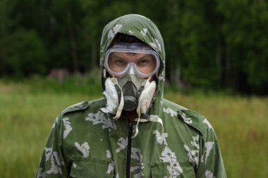 Bir adam bir maske ve gözlük ve bir kamuflaj doğa arka planı uygun. Kimyasal orduları.
