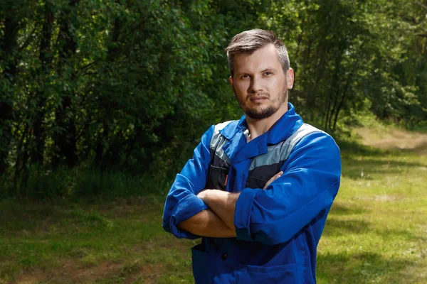 A man builder in a robe, overalls against the background of a green forest. copy space.