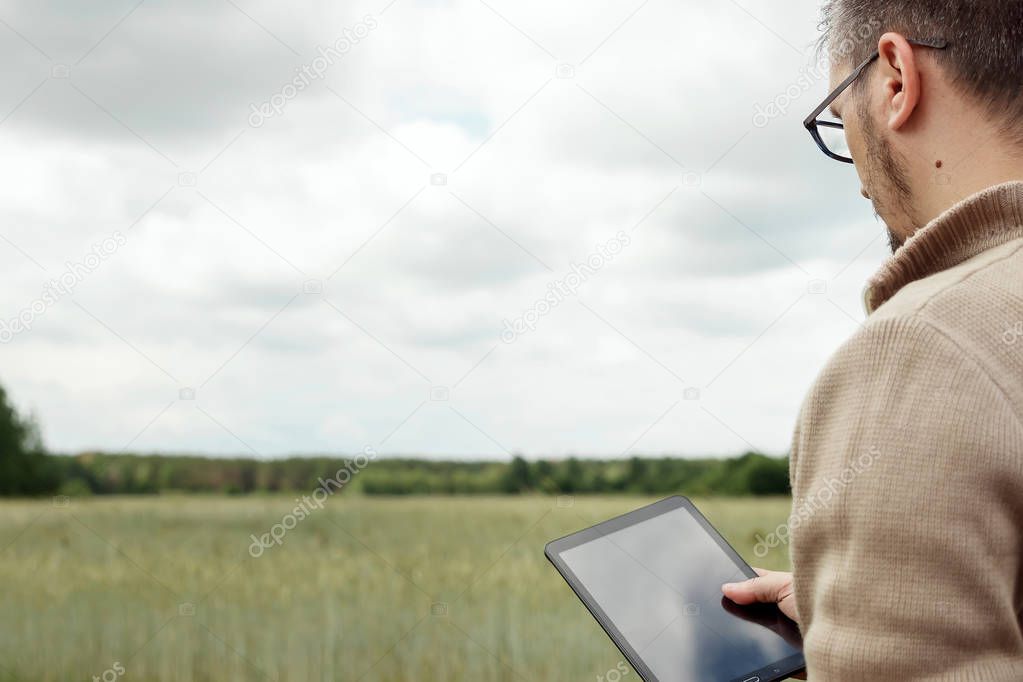 Man A farmer standing in the field and using a tablet. Modern application of technologies in agricultural activities. Farmland, new technologies, harvesting, fertilization, crop inspection.