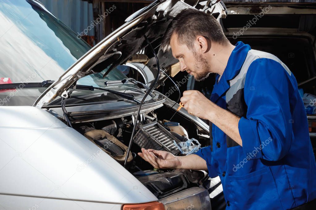 Male hands close-up, checks the oil level in the engine. The auto mechanic works in the garage. Repair service. Maintenance of the car, car repair.