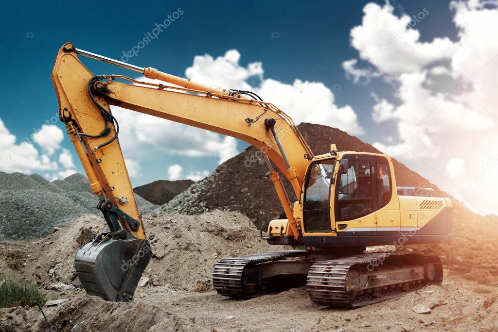 Excavator at the construction site, sand, crushed stone, against the blue sky background. Construction equipment, construction.