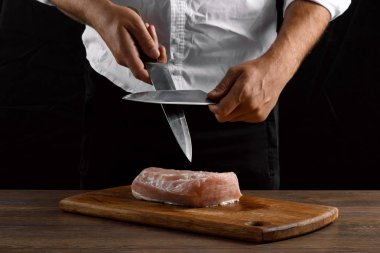 Şef closeup elinde bir bıçak karanlık bir arka plan üzerinde bir mutfak bıçağı keskinleştirir. Yemek, yemek, yemek tarifi yemekler kavramı.