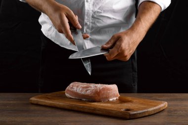 Şef closeup elinde bir bıçak karanlık bir arka plan üzerinde bir mutfak bıçağı keskinleştirir. Yemek, yemek, yemek tarifi yemekler kavramı.