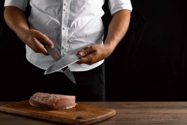 Şef closeup elinde bir bıçak karanlık bir arka plan üzerinde bir mutfak bıçağı keskinleştirir. Yemek, yemek, yemek tarifi yemekler kavramı.