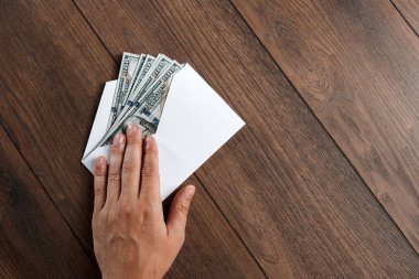 Adamın el ve beyaz bir zarf, ahşap bir masa üzerinde üstten görünüm ABD'de dolors. Gelir, ikramiye ya da rüşvet kavramı. Yolsuzluk, maaş, ikramiye.
