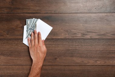 Adamın el ve beyaz bir zarf, ahşap bir masa üzerinde üstten görünüm ABD'de dolors. Gelir, ikramiye ya da rüşvet kavramı. Yolsuzluk, maaş, ikramiye.