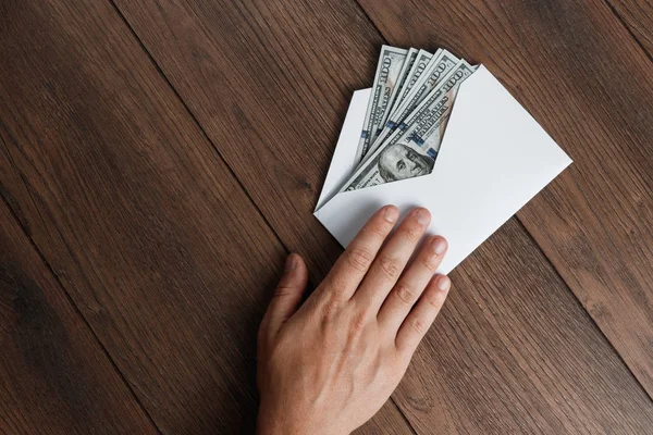 Adamın el ve beyaz bir zarf, ahşap bir masa üzerinde üstten görünüm ABD'de dolors. Gelir, ikramiye ya da rüşvet kavramı. Yolsuzluk, maaş, ikramiye.