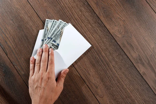Adamın el ve beyaz bir zarf, ahşap bir masa üzerinde üstten görünüm ABD'de dolors. Gelir, ikramiye ya da rüşvet kavramı. Yolsuzluk, maaş, ikramiye.