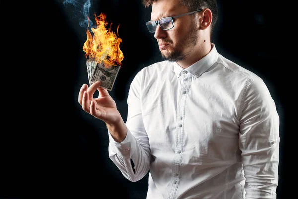 A man holds burning money in his hands, burning US dollars. The concept of inflation, a decrease in the purchase of foreign currency, and devolution.