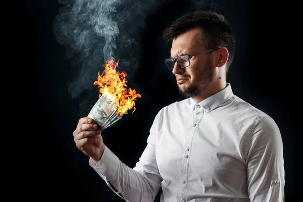 A man holds burning money in his hands, burning US dollars. The concept of inflation, a decrease in the purchase of foreign currency, and devolution.