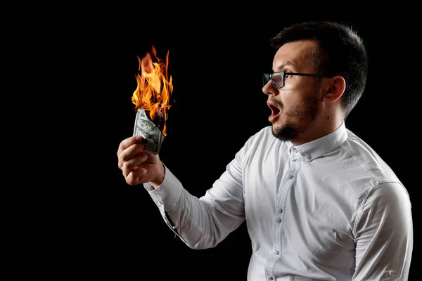 A man holds burning money in his hands, burning US dollars. The concept of inflation, a decrease in the purchase of foreign currency, and devolution.