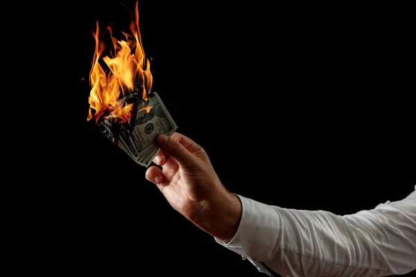 Male hand close-up, holds burning money in hands, burning US dollars. Black background, isolate. The concept of inflation, a decrease in the purchase of foreign currency, and devolution.