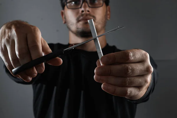 The man on a dark background cuts the cigarette with scissors. The concept of quitting smoking, giving up a bad habit.