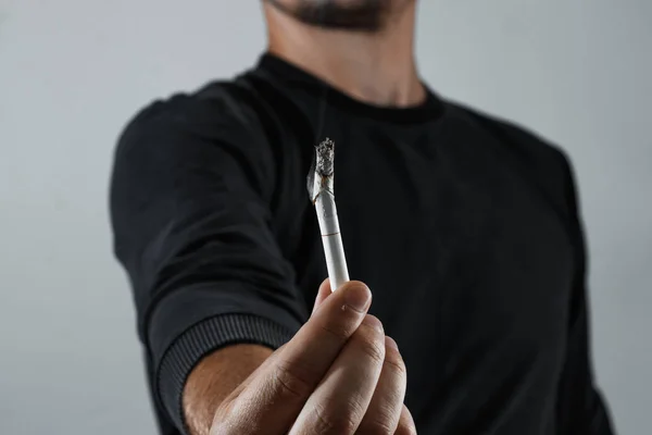 一个男人手里拿着一根烟 抽着非常近的烟 吸烟的概念 一个年轻人的手指之间燃烧的香烟是浅的 一个领域的深度副本 — 图库照片
