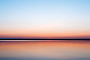 Güzel, kırmızı şafak göl kenarında. Sis sayesinde güneş ışınları. Göl üzerinde mavi gökyüzü, sabah geliyor, orman suya yansıyan.